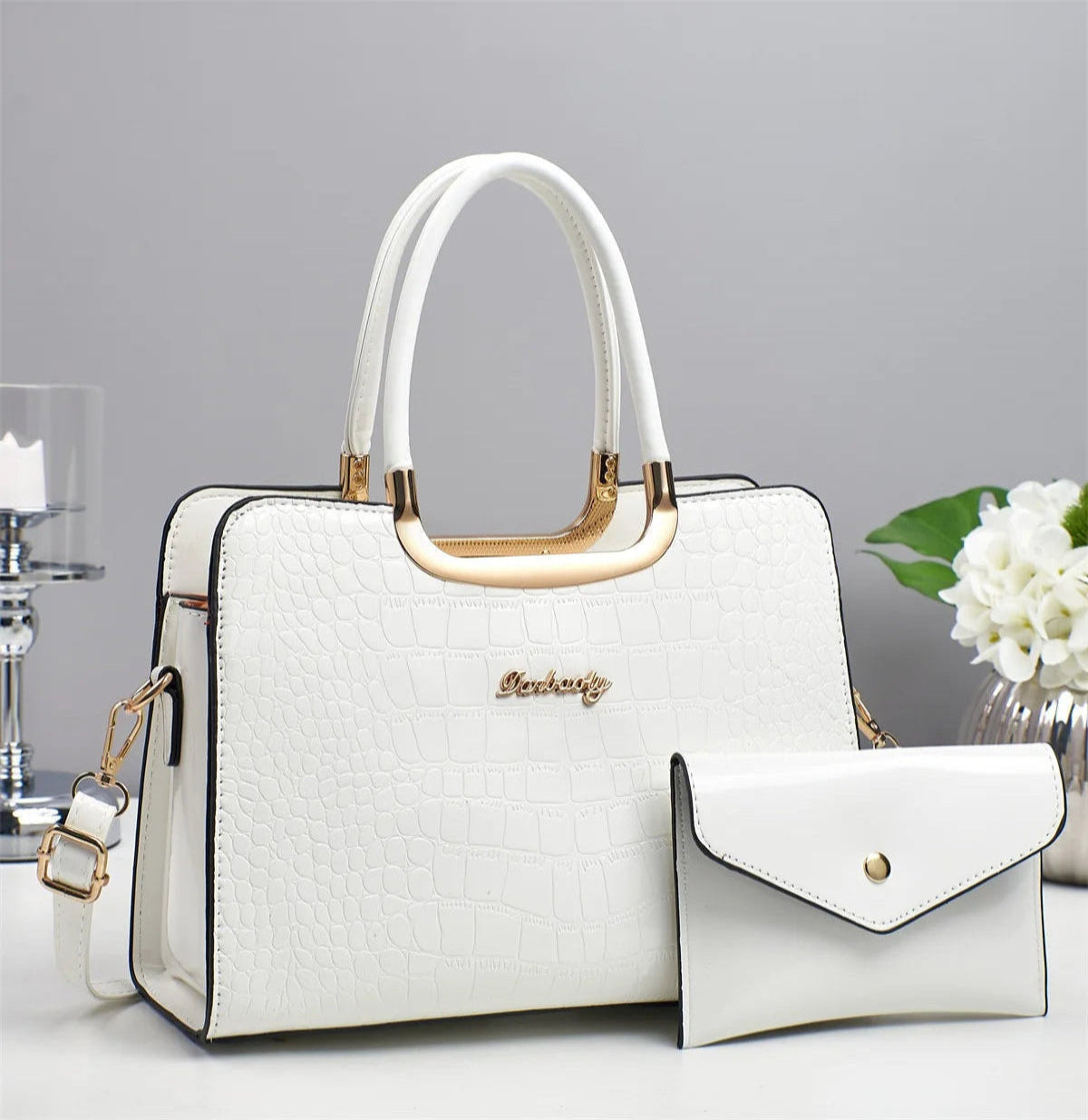 White handbag with gold accents and a matching pouch on a light gray background
